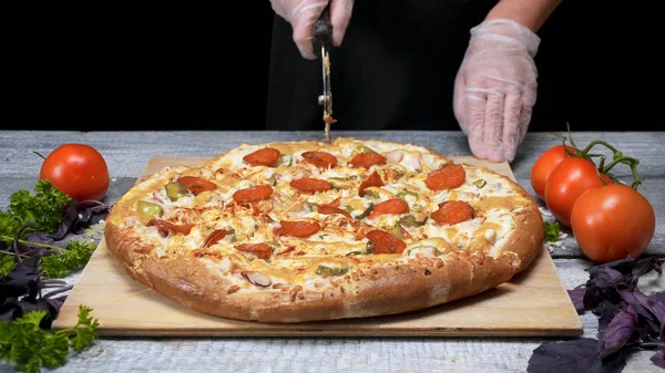 Кук режет пиццу роллерножом. Рамка. Шеф-повар перчатки вырезать роллер нож свежеиспеченные пиццы. Резка вкусной пиццы перед подачей — стоковое фото