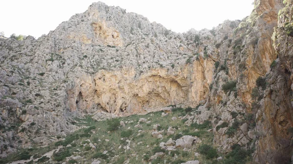 Bottom View van Cliff op achtergrond van de hemel. Kunst. Omringd door rotsachtige berg met groen te voet en schaars struiken op achtergrond van de hemel — Stockfoto