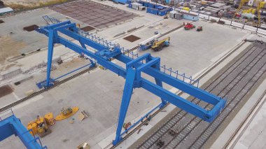 Raylar ve beton temel üzerinde duran mavi dev gantry vinç için hava. Klip. Makineler, konteynerler ve çalışan kişilerle deponun en iyi görünümü.