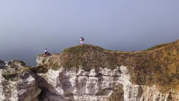 青空の背景、ライフスタイルコンセプトの白い崖の端に一緒に旅行するカップル。アクション。海の素晴らしい景色を望む丘の上の若いカップル. — ストック動画