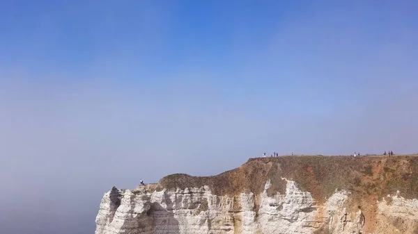 Vista aérea de un hermoso acantilado blanco sobre un fondo de cielo azul nublado, atracción de viaje. Acción. Gigante roca escarpada sobre el mar tranquilo con gente caminando en su cima . —  Fotos de Stock