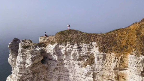 Casal viajando juntos na borda do precipício branco no fundo do céu azul, conceito de estilo de vida. Acção. Jovem casal de viajantes em uma colina com vistas deslumbrantes do oceano . — Fotografia de Stock