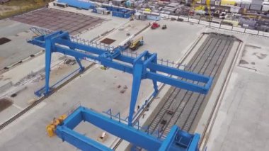 Raylar ve beton temel üzerinde duran mavi dev gantry vinç için hava. Klip. Makineler, konteynerler ve çalışan kişilerle deponun en iyi görünümü.