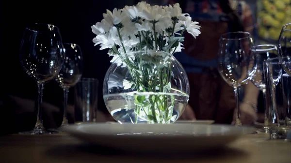 La mujer pone jarrón de flores en la mesa. Acción. Primer plano de la mujer pone jarrón de flores blancas en la mesa de servicio con luces misteriosas en el fondo oscuro — Foto de Stock