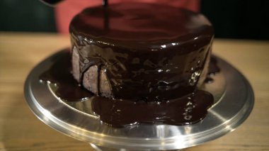 Kekin üzerine dökülen sıvı çikolatanın yakın çekim. Eylem. Eritilmiş sıvı çikolata demir standı üzerinde yuvarlak kek üzerine yayılır. Çikolata şurubu ile kaplama kek. Şekerleme ve pişirme