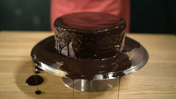 케이크에 액체 초콜릿을 클로즈업. 작업. 녹인 액체 초콜릿은 철제 스탠드에 둥근 케이크 위에 퍼져 있습니다. 초콜릿 시럽코팅 케이크. 제과 및 베이킹 — 스톡 사진