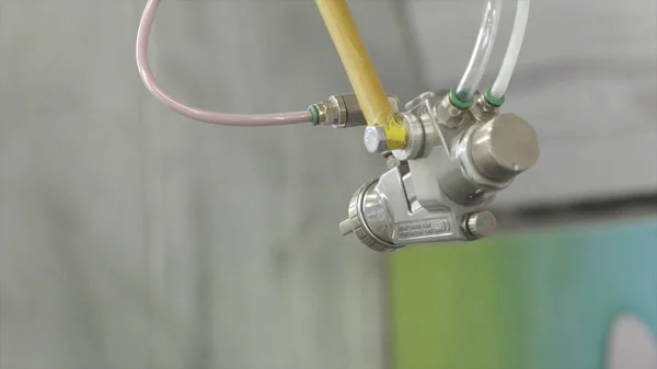 Spray gun with paint in automated production. Action. Close-up automatic with robot hand spray working with painting parts in factory production. Automated high technologies in production