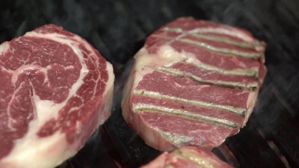 Primer plano de trozos de carne roja en la parrilla. Acción. Trozos de jugosa carne de mármol se fríen en la parrilla negra abierta. Comida, barbacoa jugosa con calidad y carne jugosa — Foto de Stock