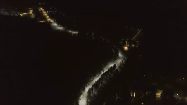 Вид сверху на зимнюю дорогу в лесном массиве ночью. Клип. Заснеженная дорога, освещенная фонарями ночью — стоковое фото