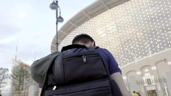 Jovem com mochila preta andando na cidade. Acção. Visão traseira de cara confiante cruzando estrada com mochila preta indo ao estádio na cidade — Fotografia de Stock