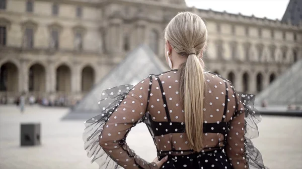 Jovem caminha no Louvre no verão. Acção. Senhora bonita em roupa elegante feliz caminha ao longo da praça do Louvre, desfrutando de férias de verão — Fotografia de Stock