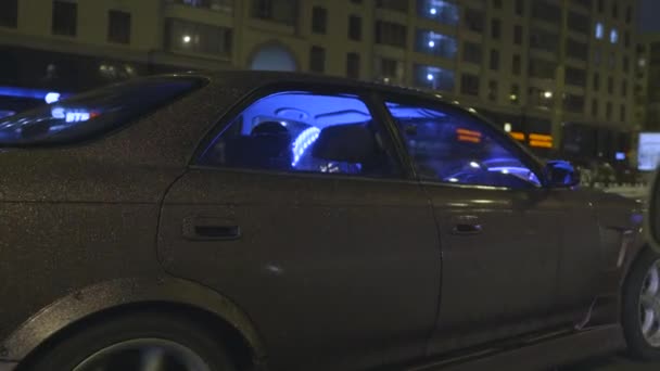 Vista lateral de um veículo moderno com belo corpo de carro roxo brilhante cobrindo se movendo rápido na cidade à noite. Acção. Carro de passageiros sintonizado com luz azul néon dirigindo ao longo das ruas . — Vídeo de Stock