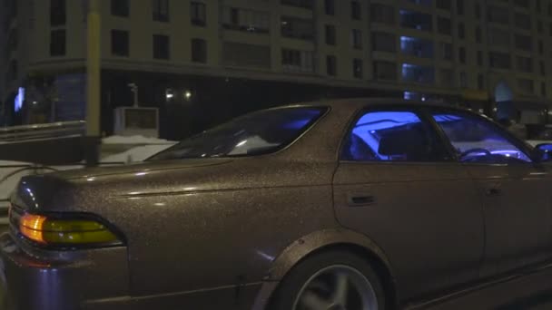 Oldalnézetből egy modern jármű gyönyörű lila csillogó autó test, amely gyorsan mozog a városban éjjel. Akció. Hangolt személygépkocsi neon kék fény vezetés az utcákon. — Stock videók