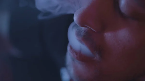 Close-up voor de man het roken van een waterpijp, uitademen rook op donkere achtergrond, slechte gewoonten concept. Actie. Portret van een jonge man in rook van elektronische sigaret of Vape. — Stockfoto