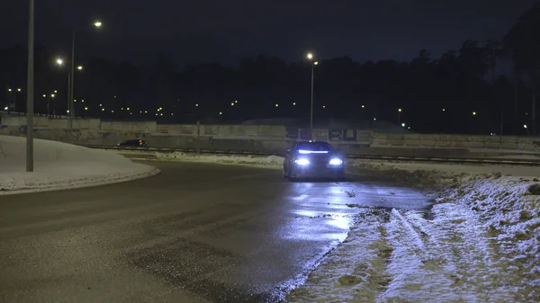 Auto parcheggiata sulla strada innevata vuota di notte con i fari accesi. Azione. Auto solitaria con fari al neon in piedi sulla strada al buio . — Foto Stock