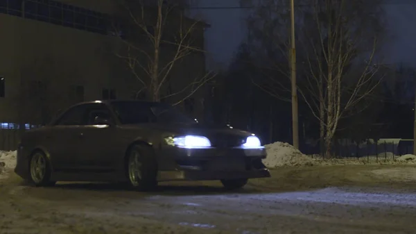 Coche de pasajeros a la deriva en una carretera nevada en la calle de la ciudad por la noche, carrera peligrosa. Acción. Un coche que va en un derrape mientras se da vuelta en la oscuridad . — Foto de Stock