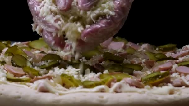 Близько до рук у кулінарних рукавичках посипте піцою з тертим сиром, італійською концепцією харчування. Рамка. Шеф-кухар кладе пармезан на піцу з шматочками маринованого огірка . — стокове відео