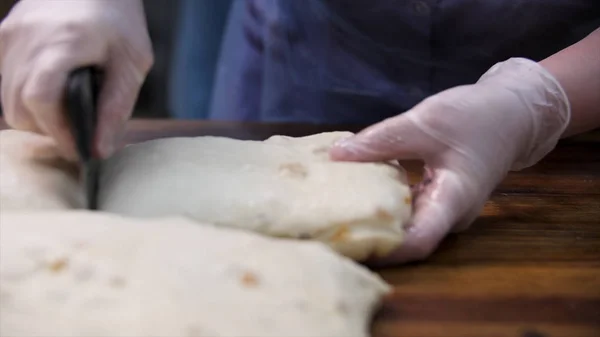 Женщина в кулинарных перчатках режет слоеное тесто изюмом на кусочки, концепция питания. Запись. Закрыть руки для резки свежего теста специальным ножом . — стоковое фото