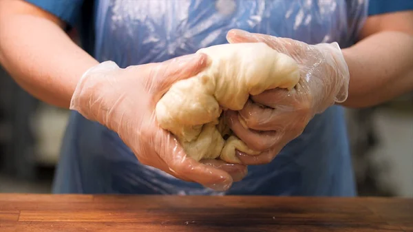 Cerrar para el confitero en el trabajo con la masa cruda con pasas. Imágenes de archivo. Cierre para las manos de la mujer en guantes de cocina tomando un gran pedazo de masa, haciendo bollos de masa . — Foto de Stock