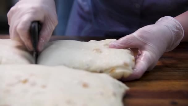 Kvinna i matlagning handskar skära smördeg med russin i bitar, matkoncept. Stock film. Närbild för händer skära färsk deg med en speciell kniv. — Stockvideo