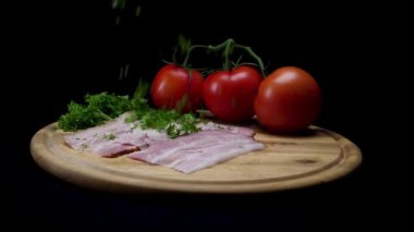 Siyah arka planda izole Prosciutto, olgun domates ve yeşilliklerle taze dilimleri ile ahşap bir tahta üzerinde düşen yeşil maydanoz için yakın. Çerçeve. Lezzetli meze, sebze, et ve baharatlar.