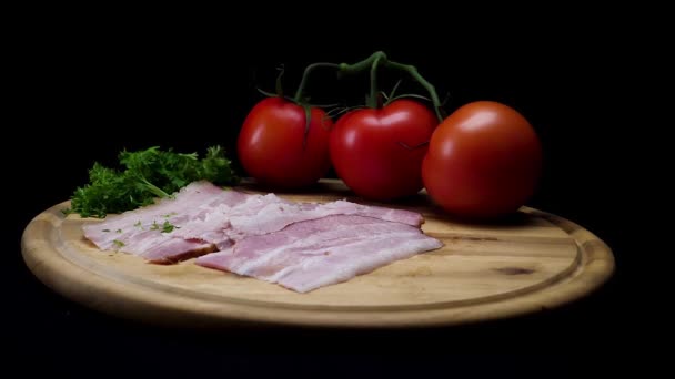 Close-up voor een houten bord met verse plakjes prosciutto, rijpe tomaten en groen geïsoleerd op zwarte achtergrond. Frame. Smakelijke aperitief, groenten, vlees en specerijen. — Stockvideo