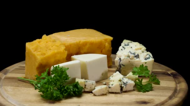 Close up for french delicious aged cheeses choped and served on wooden board isolated on black background. Frame. Cheddar, parmesan, and blue pieces of cheese with parsley. — Stock Video