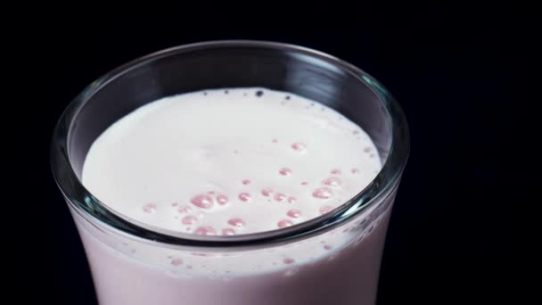 特写一杯装满草莓奶昔的玻璃,在黑色背景上隔离。框架。罐子里的粉红色冰沙,健康的夏季饮料概念. — 图库视频影像