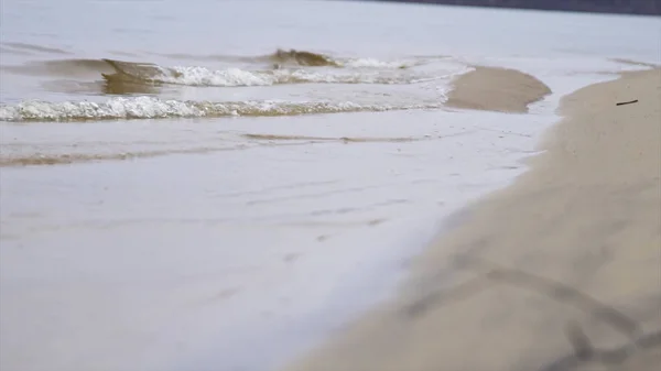 Close-up voor rivier golven op een zanderige kust. Stock footage. Kleine golven die een rivieroever wassen met licht bruin zand in een bewolkte dag. — Stockfoto