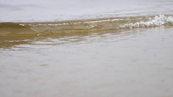 Κοντινό για τα κύματα του θαλάσσιου νερού σε μια αμμώδη παραλία, φυσικό φόντο. Υλικό από μετοχές. Μικρά κύματα πλένουν το seacoast σε μια συννεφιασμένη καλοκαιρινή μέρα. — Φωτογραφία Αρχείου