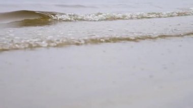 Kumlu bir kıyıdaki nehir dalgalarını kapatın. Stok görüntüleri. Küçük dalgalar bulutlu bir günde açık kahverengi kum ile bir nehir kıyısı kadar yıkama.