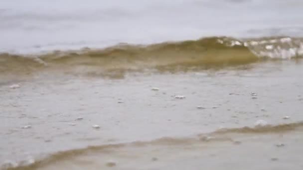 Närbild för havsvatten vågorna på en sandstrand, natur bakgrund. Stock film. Små vågor diska havskusten i en molnig sommardag. — Stockvideo