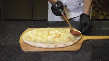 Şefin yakın çekim restoranında lezzetli İtalyan pizzası hazırlar. Çerçeve. Şef pişmiş yuvarlak pizza tabanına domates sosu döker. Ahşap tepside fırında pişirilen pizza