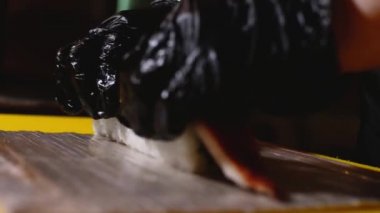 Balıkla suşi rulosu hazırlayan şefin yakın çekim. Çerçeve. Eldiven profesyonel şef suşi rulo üzerinde geyik balığı parçası koyar. Estetik ve lezzetli suşi rulo hazırlanması