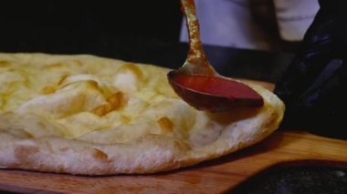 Şef domates sosu pizza sulama. Çerçeve. Şefin yakın çekim İtalyan pizza üzerine domates sosu kepçe döker. Geleneksel İtalyan pizzası hazırlığı. Pişirme kavramı