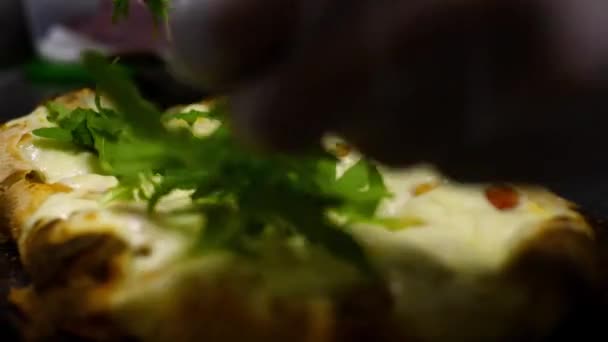 Chef-kok decoreert pizza met greens. Frame. Close-up van de chef zet salade van rucola gieten op afgewerkte pizza. Kleine pizza met kaas versierd met groene bladeren door chef-koks recept — Stockvideo