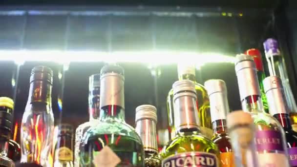 Close-up de variedade de álcool no bar. Moldura. Garrafas de vidro coloridas ficam no balcão de bar no fundo de lâmpadas brilhantes. Diferentes tipos de álcool no pub noturno — Vídeo de Stock