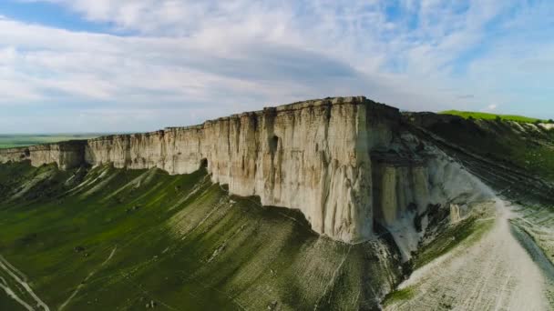 Вид зверху на красивий білий камінь з зеленою травою на тлі блакитного неба. Постріл. Панорама білої скелі з зеленим полем біля підніжжя літа — стокове відео