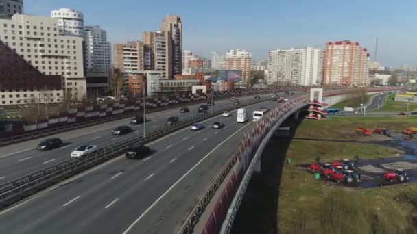 Vista superior de la carretera de la ciudad en el fondo de edificios residenciales de varios pisos. Escena. El tráfico en la carretera de la ciudad por la mañana apresurando a la gente a trabajar en el fondo de la zona residencial — Vídeo de stock