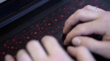 Arka ışıklı siyah klavyede yazan adamın yakın çekim. Klip. Erkek elleri modern moda klavye üzerinde yazarak. Kırmızı arka ışıklı oyun klavyesi