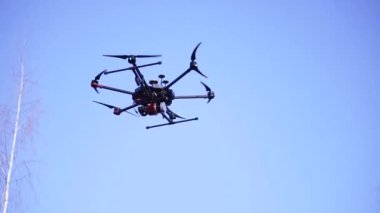 Gökyüzünde uçan quadcopter'ın yakın çekim. Klip. Arka plan mavi gökyüzünde uçan güçlü motorlar ile büyük quadcopter. Uzun hava için altı motorlu quadcopter