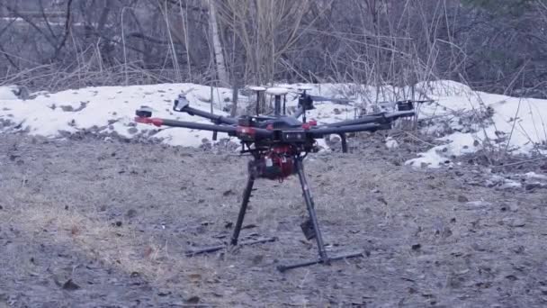 Close-up van de quadrocopter neemt af. Clip. Krachtige model van de nieuwe generatie quadcopter is op de grond voorbereiding voor het opstijgen. Quadcopter is op bos achtergrond met sneeuw — Stockvideo