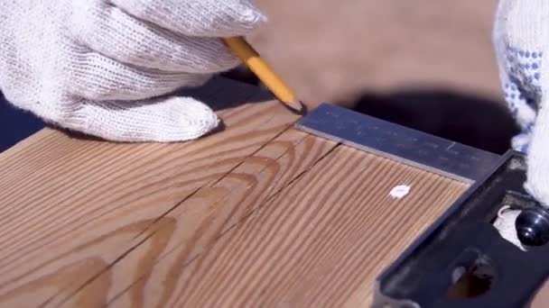 Arbetstagaren tar anteckningar om mätningar av trä ombord. Klipp. Närbild av arbetare i handskar registrerar mätningar med blyertspenna på trä kartong för sågning — Stockvideo