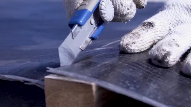 Il lavoratore taglia la copertura del tetto con un coltello. Clip. Primo piano del lavoratore in guanti con coltello taglia rivestimento in gomma sul tetto per la nuova costruzione — Video Stock