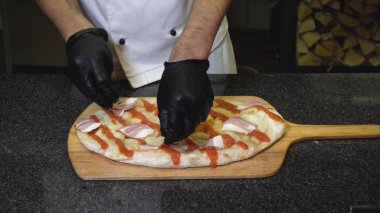 Şefin yakın çekim restoranında lezzetli İtalyan pizzası hazırlar. Çerçeve. Şef pişmiş yuvarlak pizza tabanına domates sosu döker. Ahşap tepside fırında pişirilen pizza