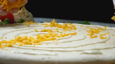 Şef pizzanın üzerine peynir döker. Çerçeve. İtalyan mutfağının profesyonel aşçısı eldivenlerle çiğ pizzanın üzerine rendelenmiş peynir döker. Siyah izole arka plan üzerinde geleneksel pizza hazırlanması