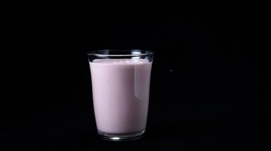 Çilek milkshake siyah arka plan üzerinde izole. Çerçeve. Pembe milkshake ile dolu şeffaf cam hareket etmeden siyah arka plan üzerinde duruyor