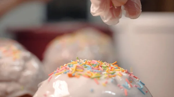 Close-up of easter cakes sprinkled with sprinkles. Stock footage. On sweet glazed white easter cakes pour rainbow sprinkles. Traditional preparation of cakes for celebration of Easter