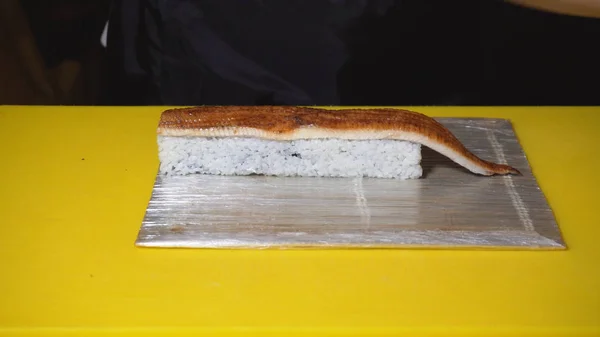 Close-up de chef preparando rolo de sushi com peixe. Moldura. Chef profissional em luvas coloca pedaço de enguia em rolos de sushi. Preparação de rolos de sushi estéticos e deliciosos — Fotografia de Stock