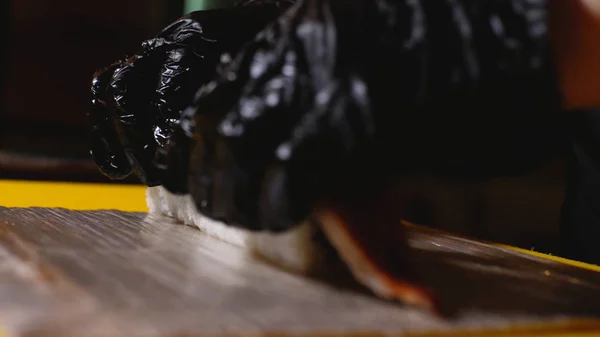 Close-up of chef preparing sushi roll with fish. Frame. Professional chef in gloves puts piece of eel on sushi rolls. Preparation of aesthetic and delicious sushi rolls
